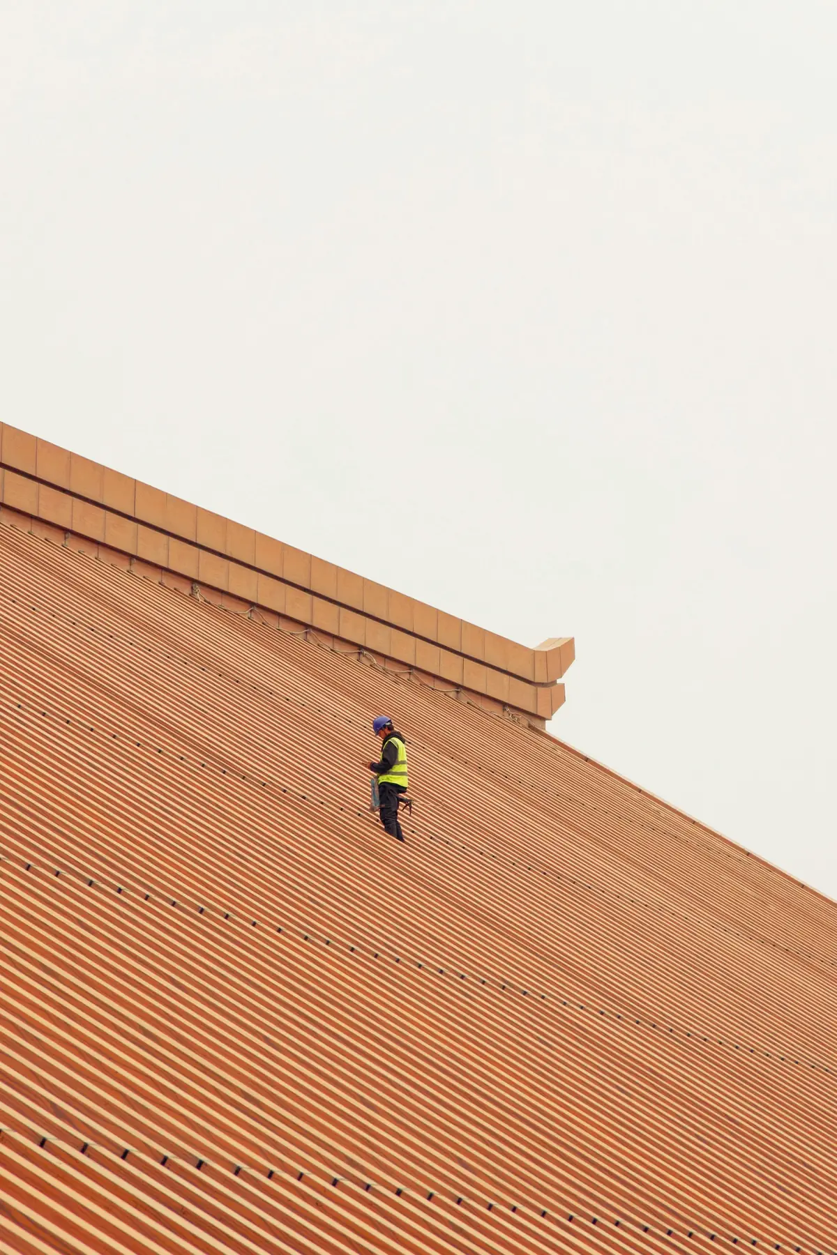 A roofer in hi-vis walking up a long run of red corrugated iron